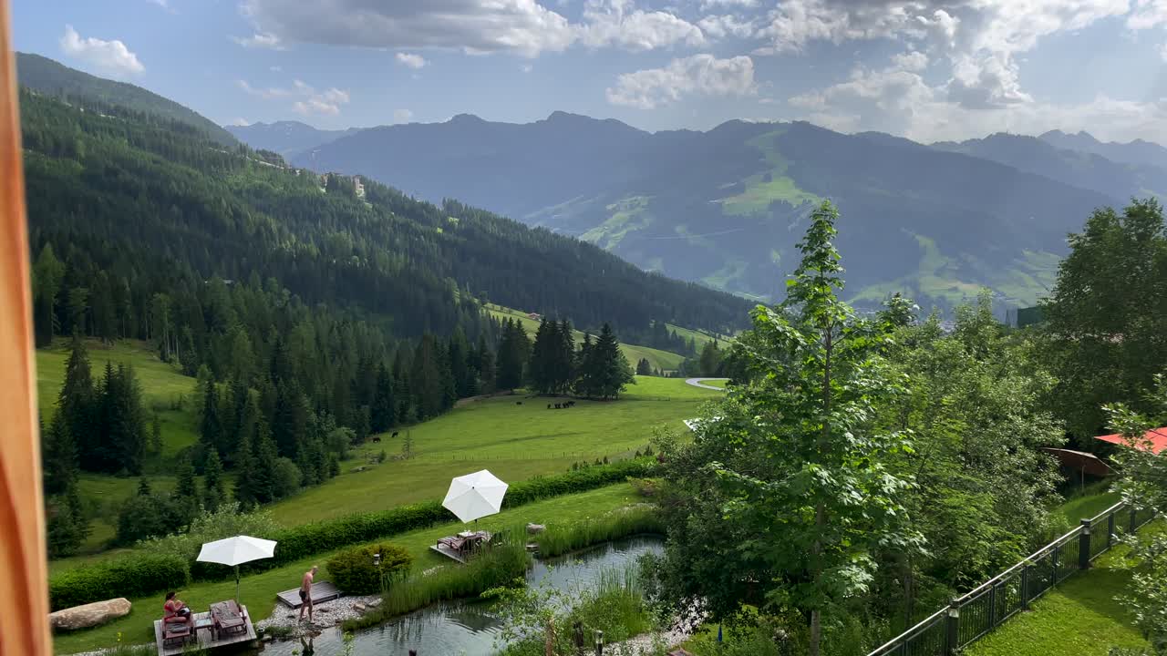 Ripresa con carrello in avanti di un balcone in un hotel resort di lusso che mostra un turista che si rilassa su un lago naturale e montagne ricoperte di vegetazione sullo sfondo.