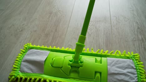 microfiber wet mop moving around the floor at home. person in slippers mopping the floor with a green brush. housework. close-up.