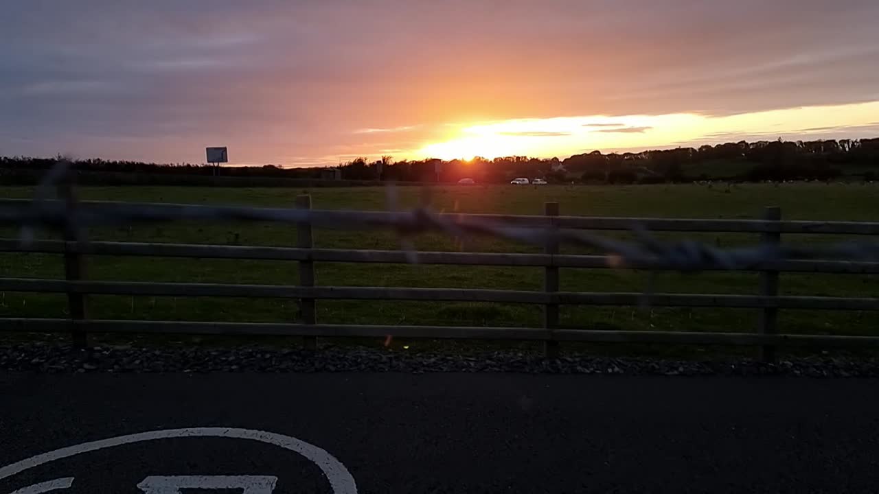 Looking through barb wire boundary fence to sunset orange skyline over agricultural rural farmland