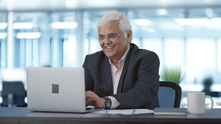 Happy senior Indian manager working on laptop