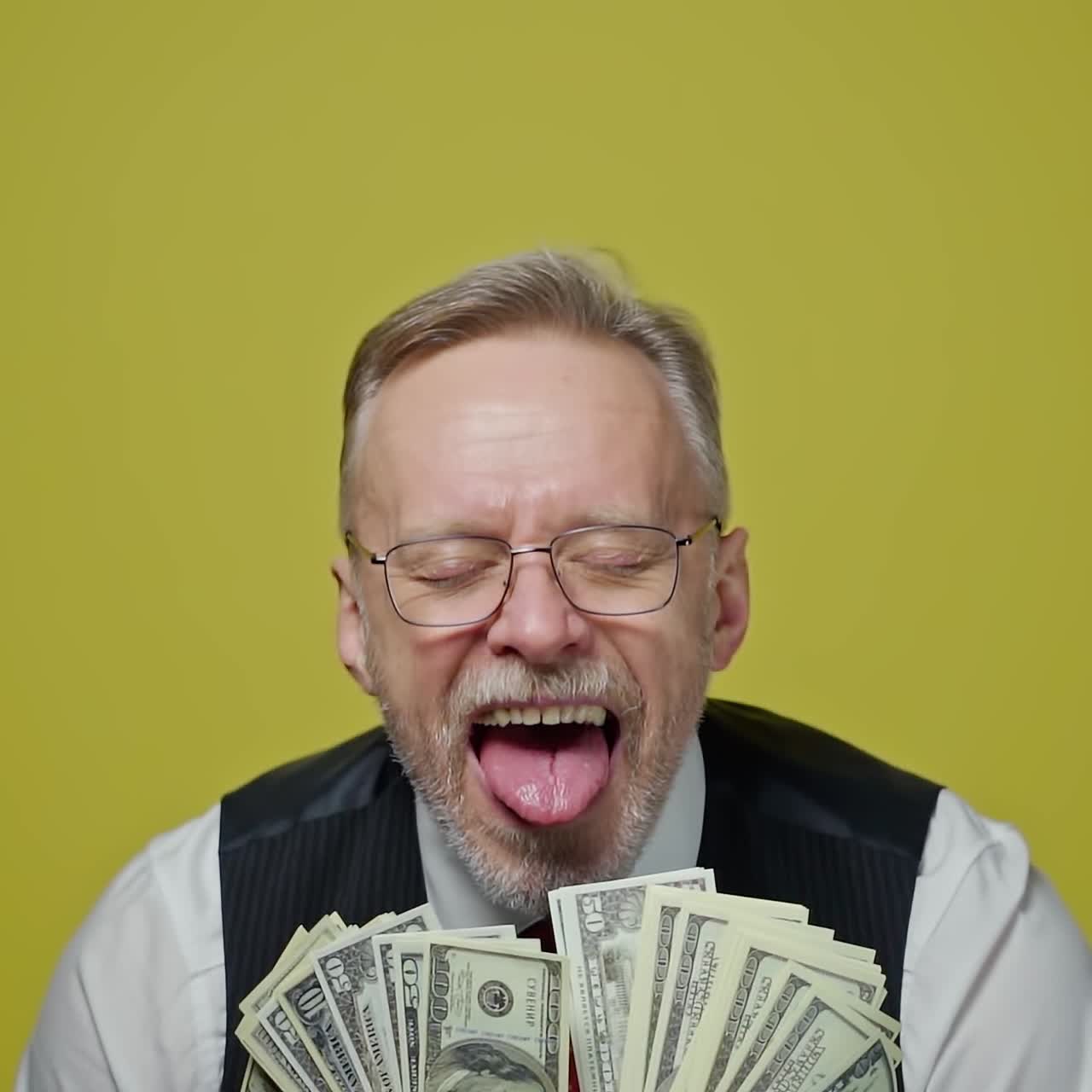 Portrait of happy senior man with money. Mature man in glasses holds many dollar bills and opens his mouth with joyfulness on yellow background. Slow motion.