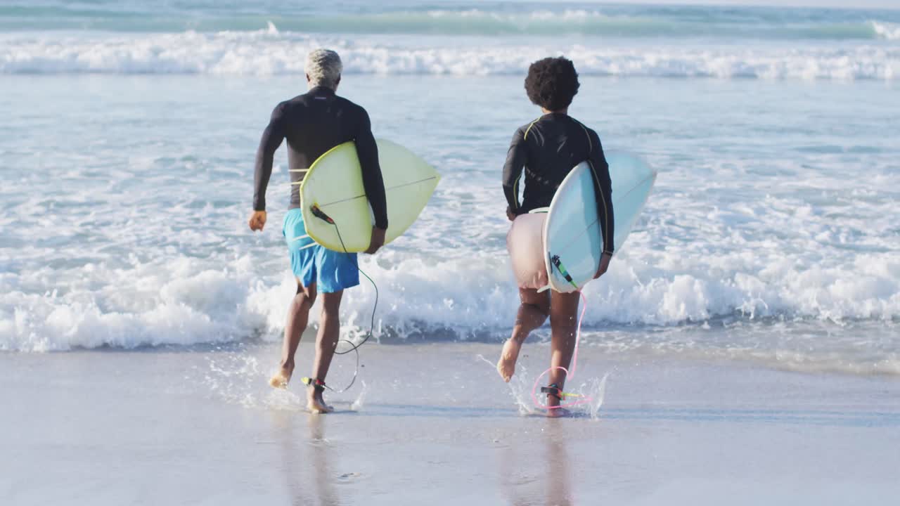 feliz pareja afroamericana corriendo con tablas de surf en una playa soleada