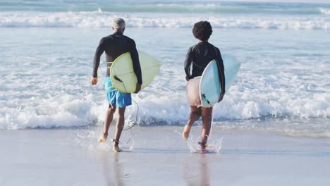 happy african american couple running with surfboards on sunny beach