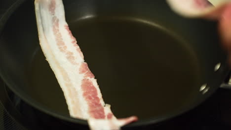 placing slices of bacon inside a pan to fry