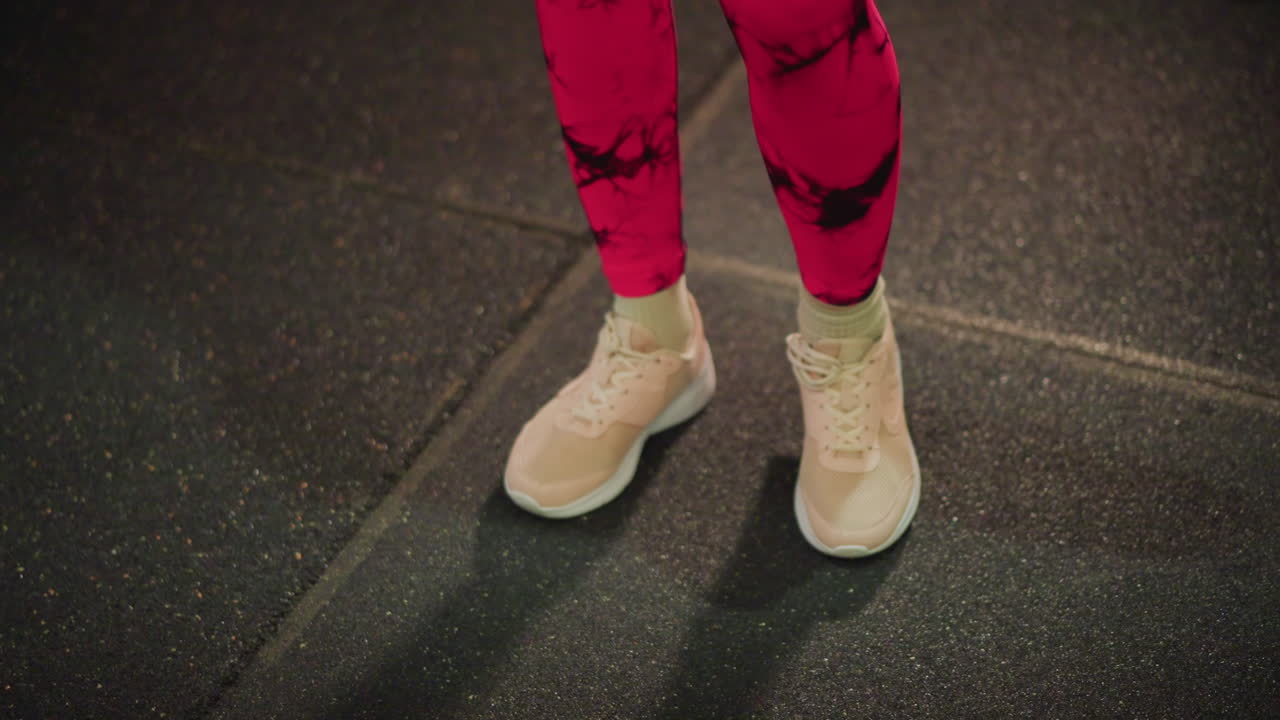 Zapatillas en una colchoneta de goma desde un ángulo bajo, leggings rosas. Atleta ajustando las posiciones del talón y la punta del pie durante un ejercicio de juego de pies, con un ritmo constante y un suelo texturizado bajo una brillante iluminación de estudio, haciendo énfasis en el equilibrio.