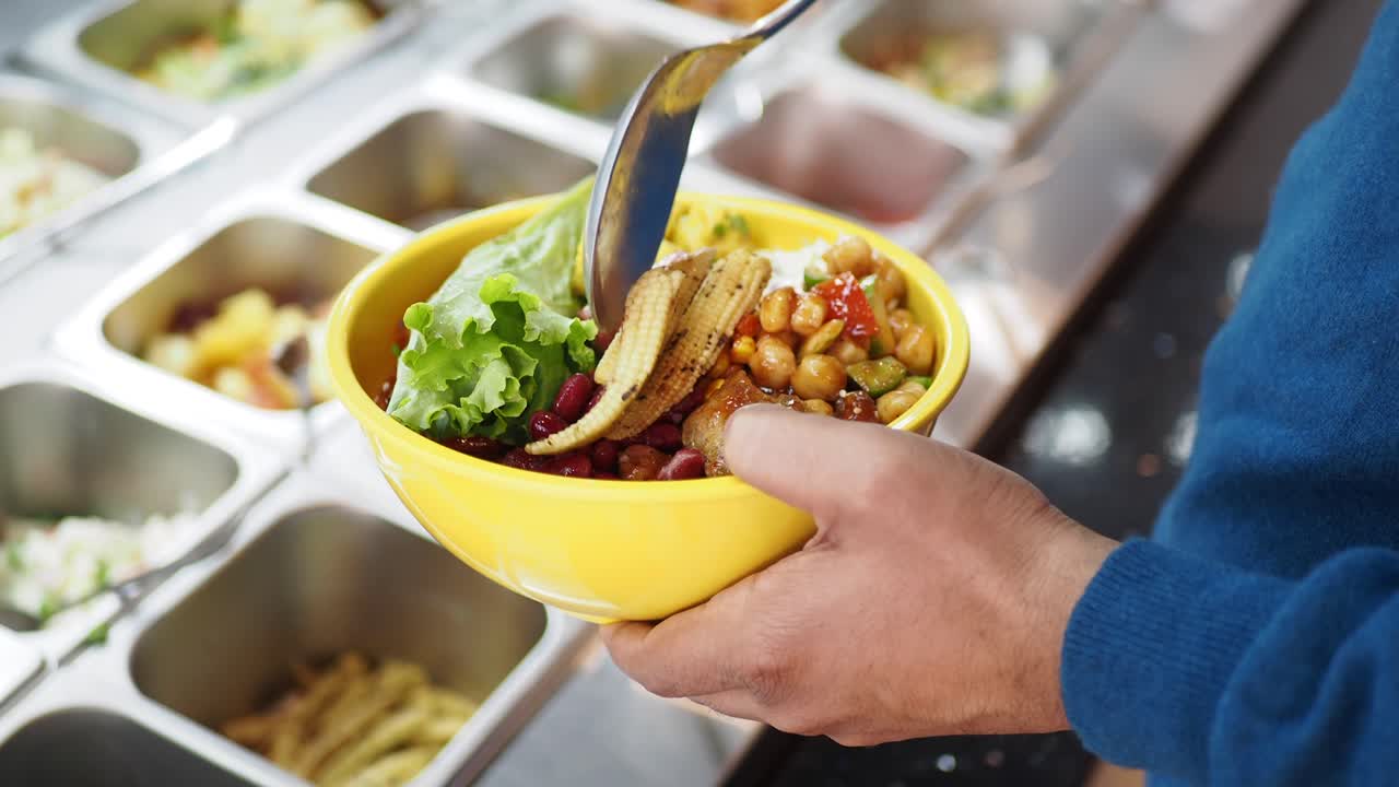 Person holding a colorful bowl of food from a self-service restaurant