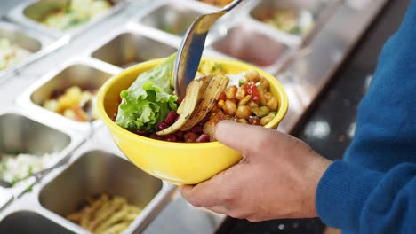 person holding a colorful bowl of food from a self-service restaurant