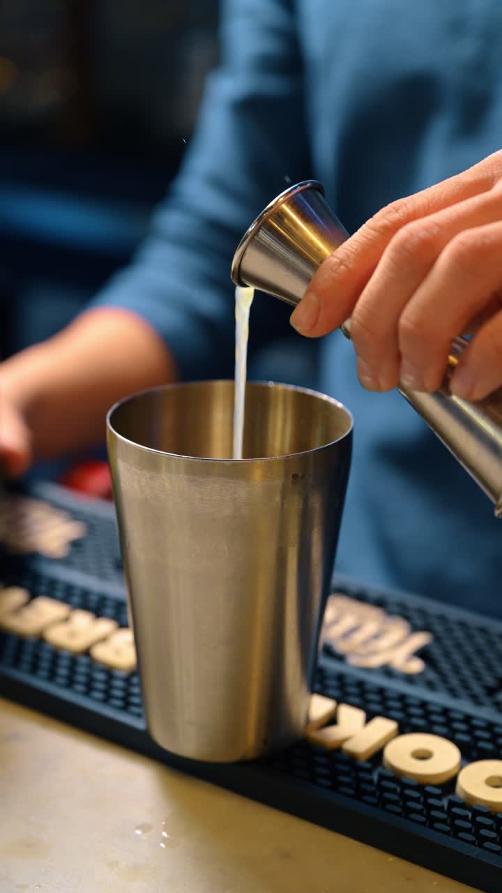 Versando liquido da un jigger in uno shaker di metallo. Primo piano di un barista che aggiunge ingredienti misurati per la preparazione di un drink
