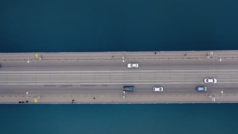 aerial top down view of bridge. cars ride on an overpass over the water. pedestrians on the bridge