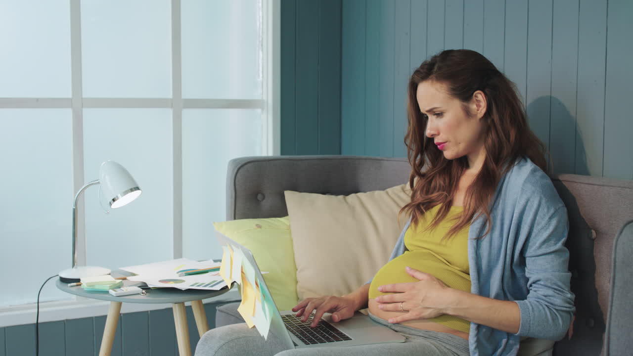 집에서 소파에서 노트북으로 일하는 아름다운 임신한 여성의 클로즈업.