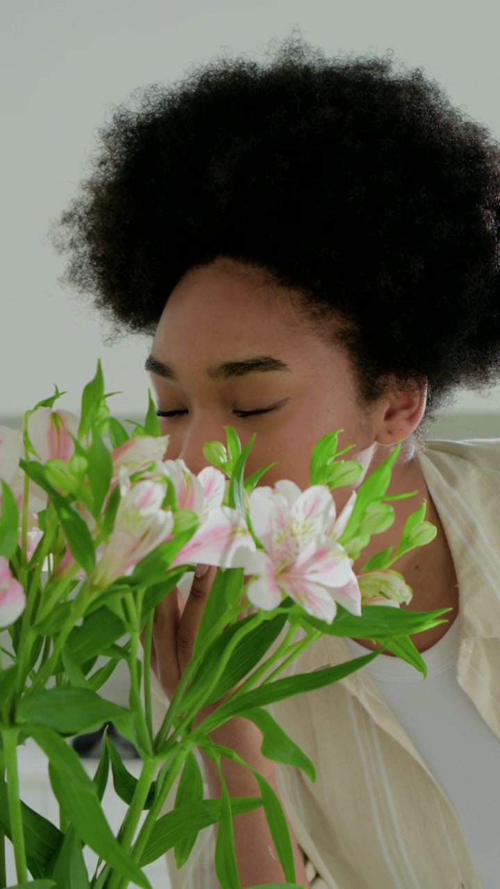 Vertikal video: Visar bukett, kvinna med kopp i beige tröja lutar sig fram och doftar på blommor i köket.