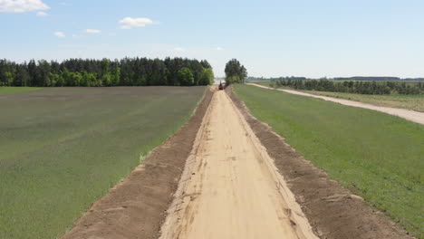 excavator digging roadbed through farmland and forest. road construction. drone approach