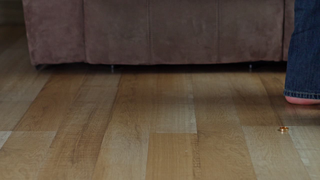 Conceptual shot of wedding ring dropped on laminate floor with person walking away in background