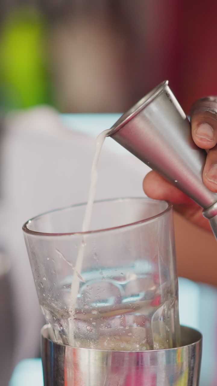 Barman pours liqueur from beaker in bar closeup. Young bartender prepares cocktail for customer in nightclub. African American man makes drink
