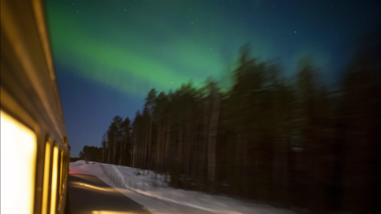 vista exterior del tren viajando a través de un bosque nevado con luces verdes del norte iluminando el cielo