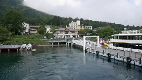 Ferry-taking-off-for-a-ride-from-a-small,-hilly-sea-port-on-a-cloudy-morning