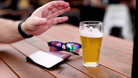 person takes a beer glass off a wooden table.