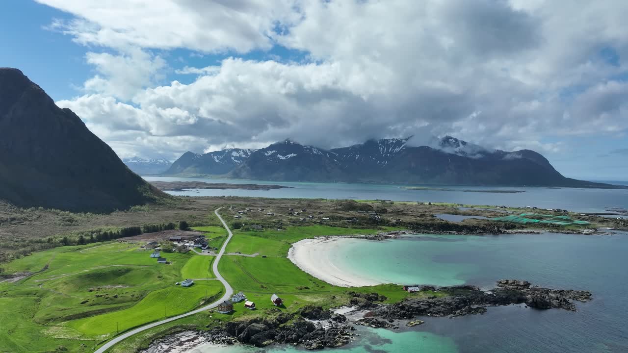 Drone flies forward over Hov beach on Gimsoy showing turquoise sea green hills road and peaks
