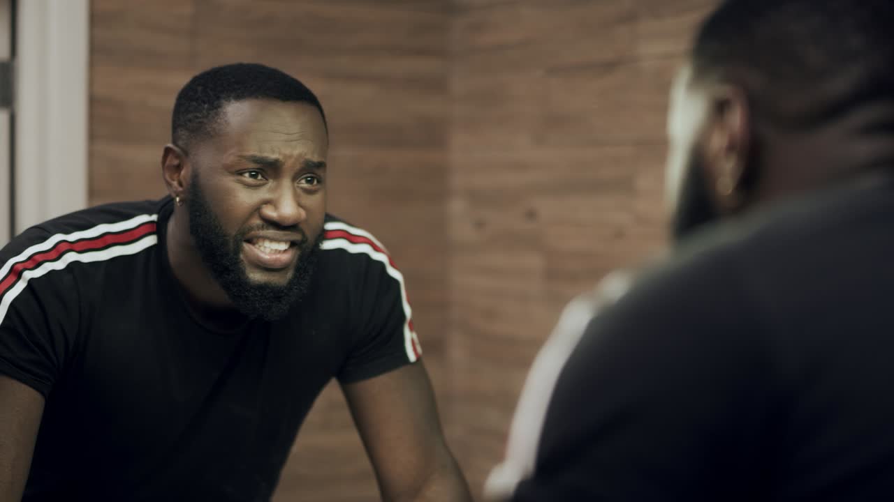 Back man sparing in front of mirror. Upset african man depressing in bathroom.