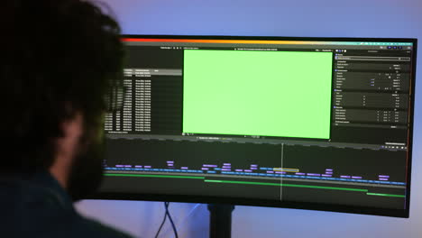 A-professional-editor-working-on-editing-program-with-green-screen,-over-the-shoulder-view