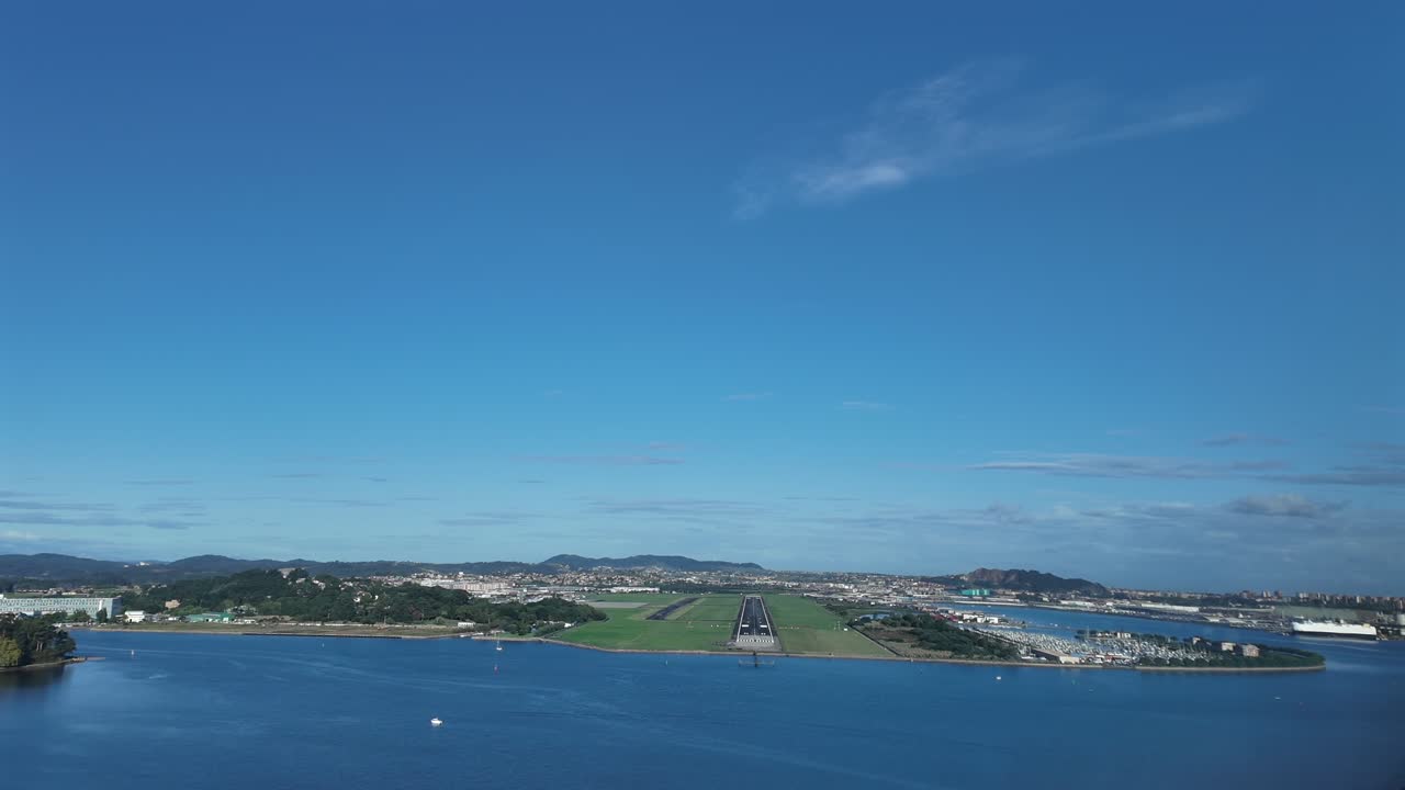 An immersive pilot’s eye from the cockpit of a jet airplane approaching to Santander airport, overflying the bay, with a far view of the city, under a blue sky with few clouds