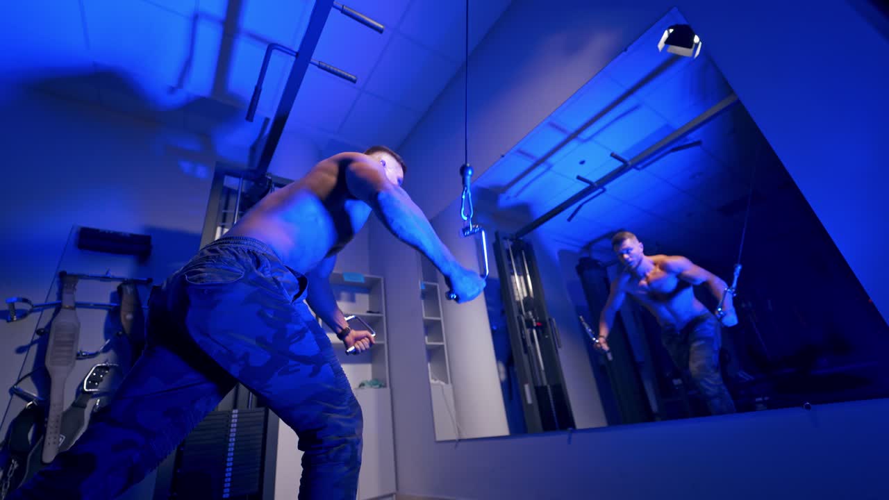 Handsome bodybuilder doing workout pushing up excercise in gym in front of the mirror. Blue light filter, Naked torso. Shirtless trainer. Video from the side.