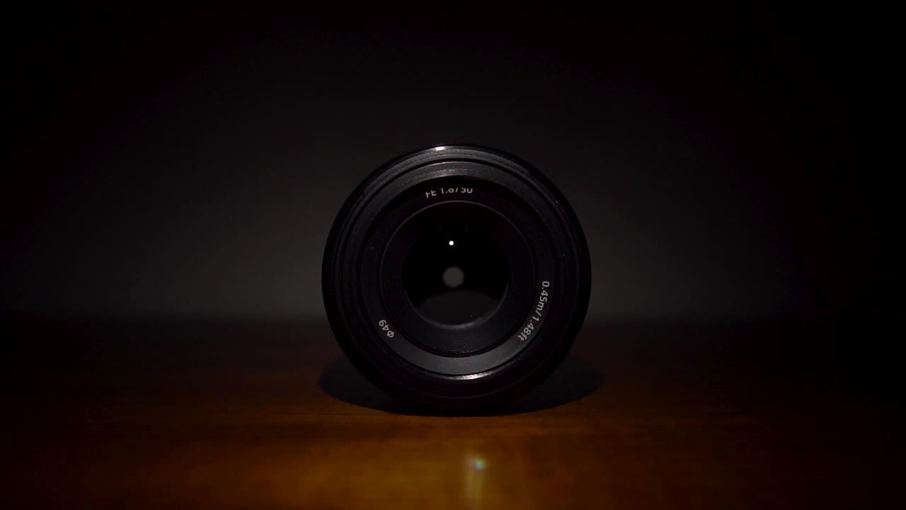 Black 50mm camera lens, glowing light reflection, isolated against dark background