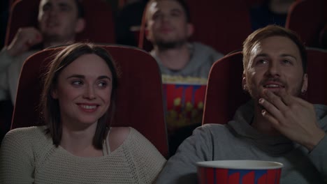 young people enjoying film in cinema. couple eating popcorn and watching movie