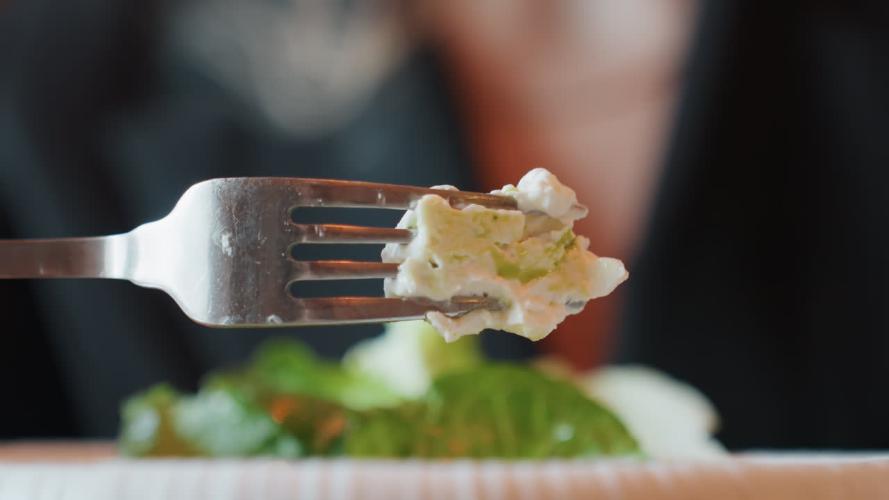 Nærbillede af gaffel med salatbid, sløret gæst i blazer på eksklusiv restaurant, sprød salat og cremet ost spiddet på tænderne, blød bokeh-baggrund, raffineret smagsatmosfære der fremkalder elegance.