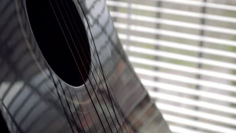 black shiny acoustic guitar on a stand by the window, close up