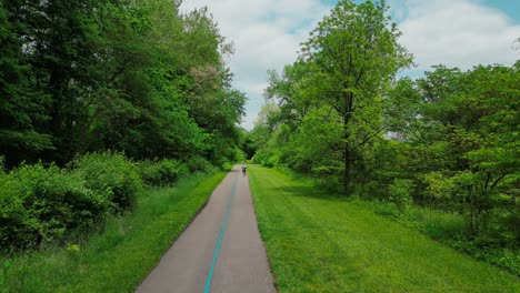 drone disparado volando sobre un camino pavimentado en el bosque del parque con un ciclista