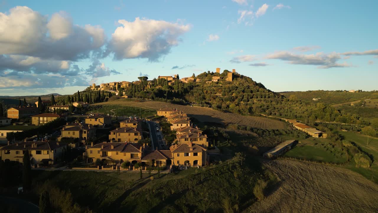 Golden hour glow on Val d'Orcia Tuscany village with orchards and farm fields, aerial panoramic