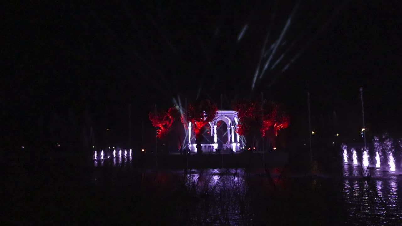 Gorgeous water colorful light show in Kadriorg park during evening in slow motion. Light beams illuminate a house in the middle and water fountains shoot up at different time with different colors.