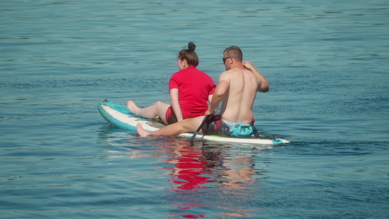Couple together on a paddleboard in calm blue sea water during a sunny day, enjoying a relaxing and active outdoor adventure on the water. Captured in slow motion