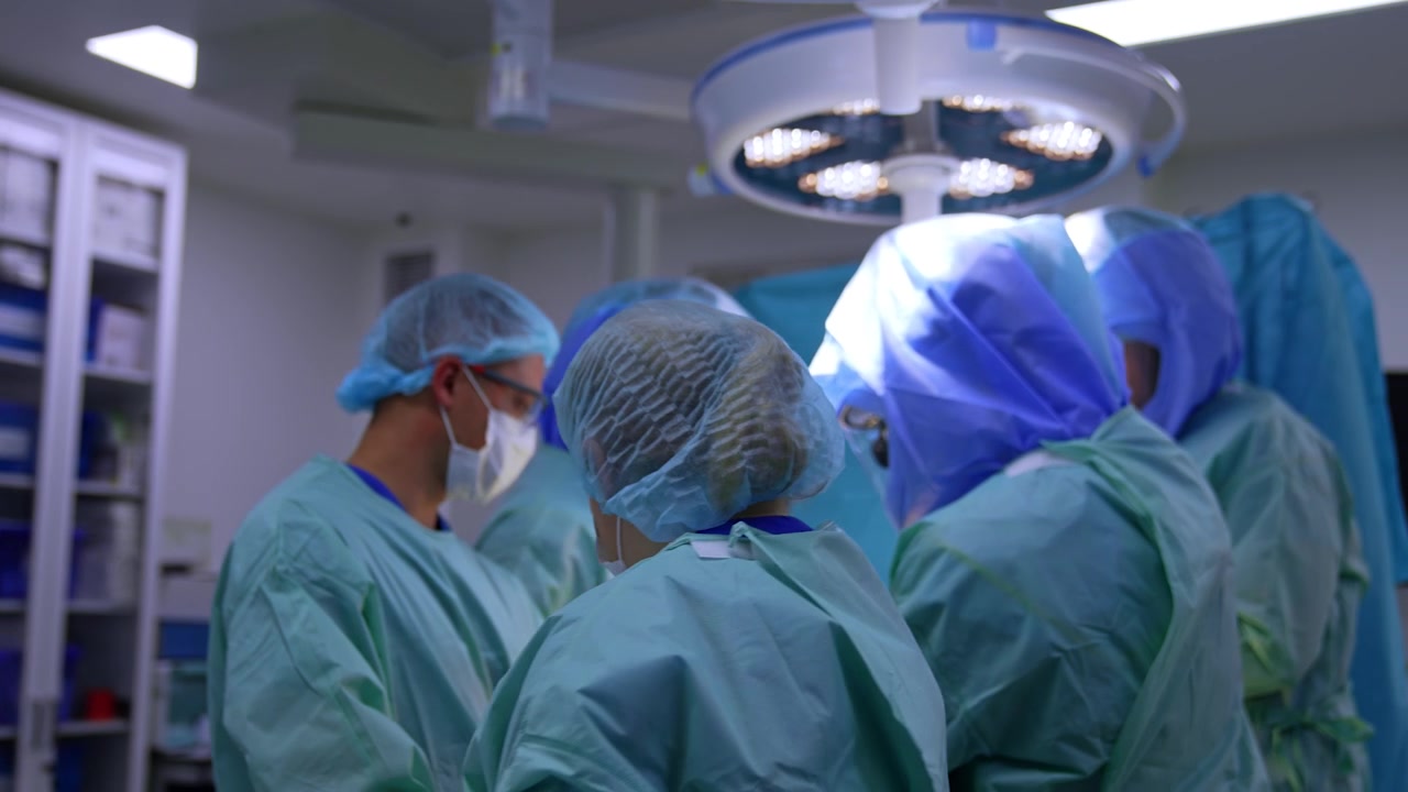 Orthopedic operation performed by a big team of doctors. Surgeons wear protective helmets at procedure.