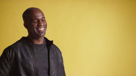 head and shoulders studio portrait of smiling and laughing mature man against yellow background 5