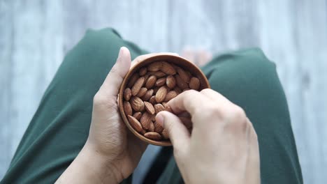 persona comiendo almendras de un cuenco de madera
