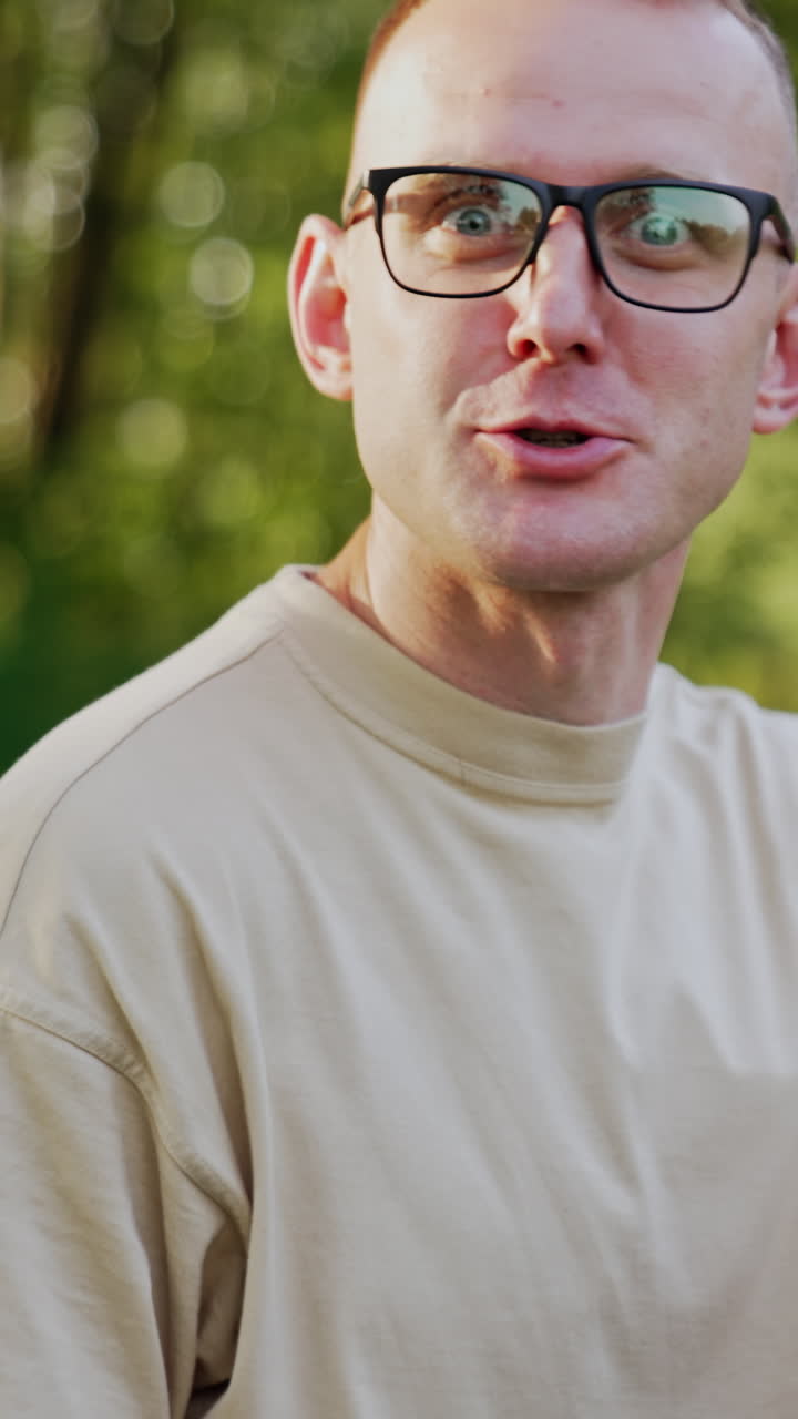 Caucasian man wearing eyeglasses works outdoors. Male freelancer talks to camera gesturing with hand. Vertical video