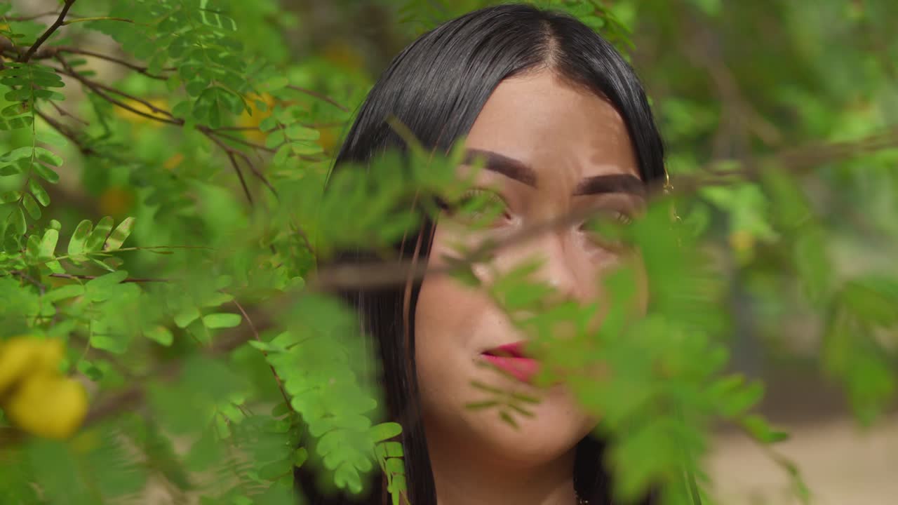 공원에서 잎 뒤에 있는 젊은 여성의 얼굴 클로즈업