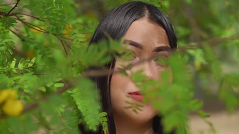 facial close up of a young woman behind leaves at a park