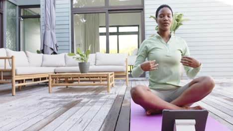 Mujer-Birracial-Enfocada-Practicando-Yoga-Y-Meditando-Con-Tableta-En-El-Jardín,-Cámara-Lenta