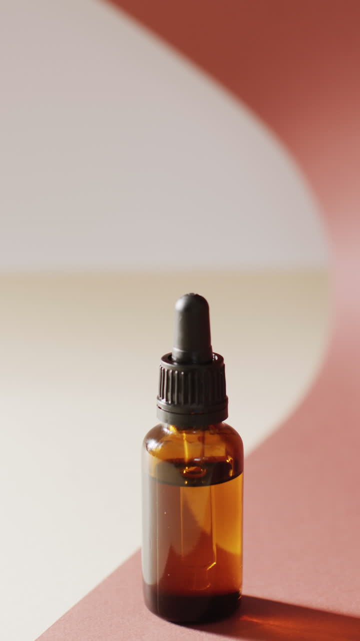Vertical video of dropper serum bottle on pink background with copy space
