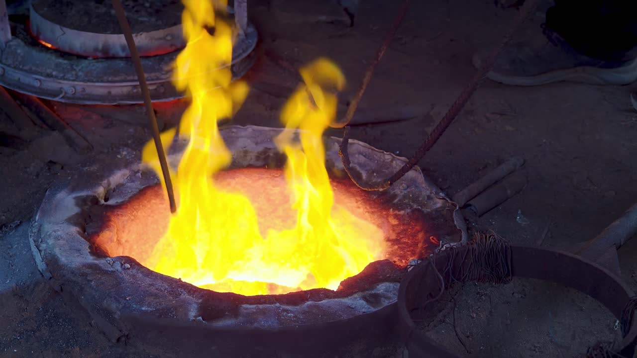 Flames rise as rods are inserted into an underground floor crucible to gather molten alloy for bell casting in a traditional foundry in Crema, Lombardy, Italy, slow motion