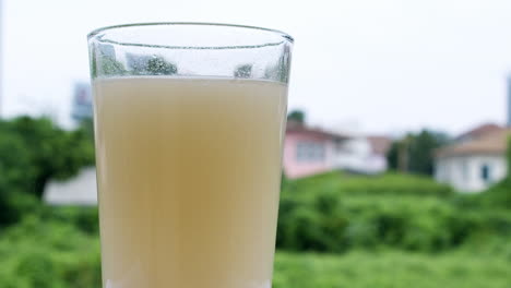 Murky-water-in-a-clear-glass-with-a-blurred-backdrop-of-houses-and-green-trees