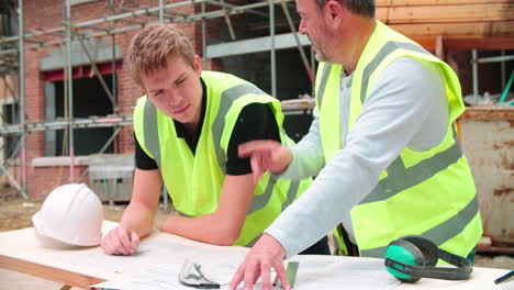 builder on building site discussing work with apprentice