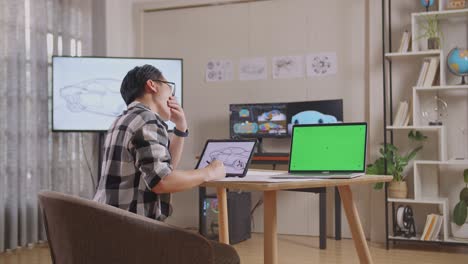 테이블릿을 에 초록색 화면 노트북과 tv와 컴퓨터를 가진 스튜디오에서 3d 전기 자동차 모델을 표시하는 동안 아시안 남성이 걱거리는 측면 뷰