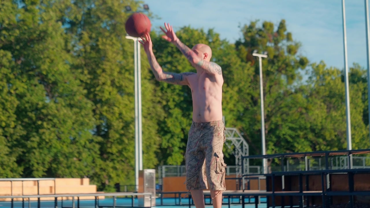 Bald Man with Tattoos Shoots Basketball on Outdoor Court