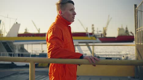 joven en uniforme naranja de pie junto a la valla y descansando durante su descanso junto al mar en el puerto