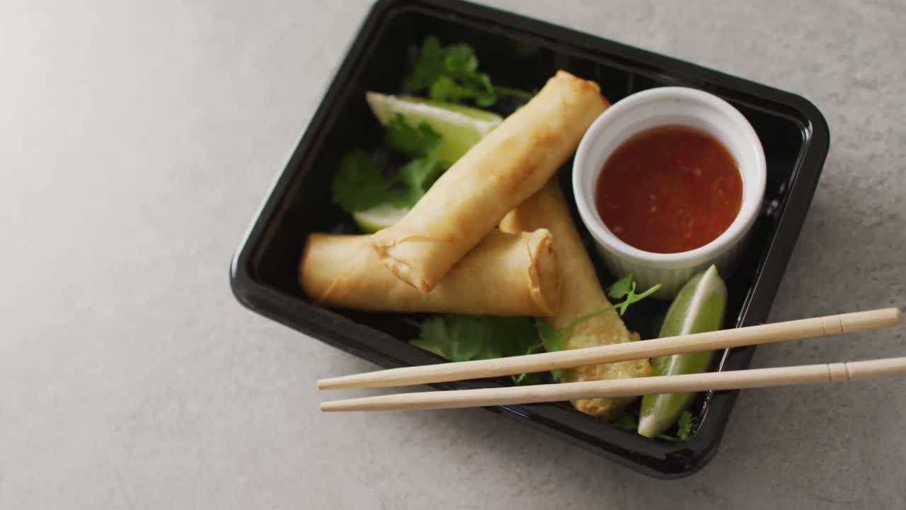 Komposisi piring dengan lumpia dan saus sambal dengan sumpit di latar belakang abu-abu