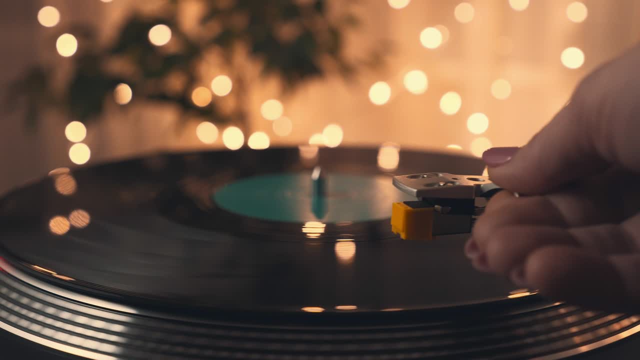 디제이 턴테이블 레코드 플레이어의 비닐 레코드 가까이. 소녀의 손은 회전하는  비닐 레코드에서 바늘로 스타일러스를 부드럽게 넣고 내려 놓습니다. 밝은 파티 불빛의 배경.